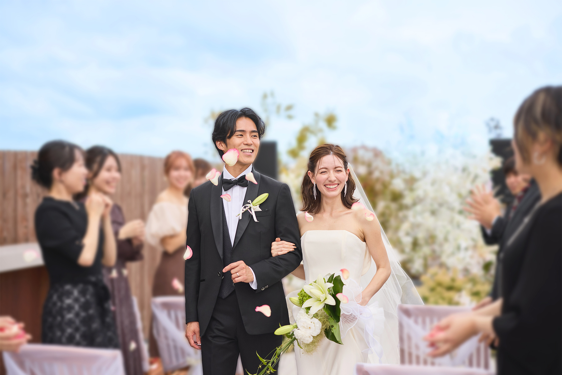 フラワーシャワーを浴び笑顔で退場する洋装の新郎新婦とゲストたち